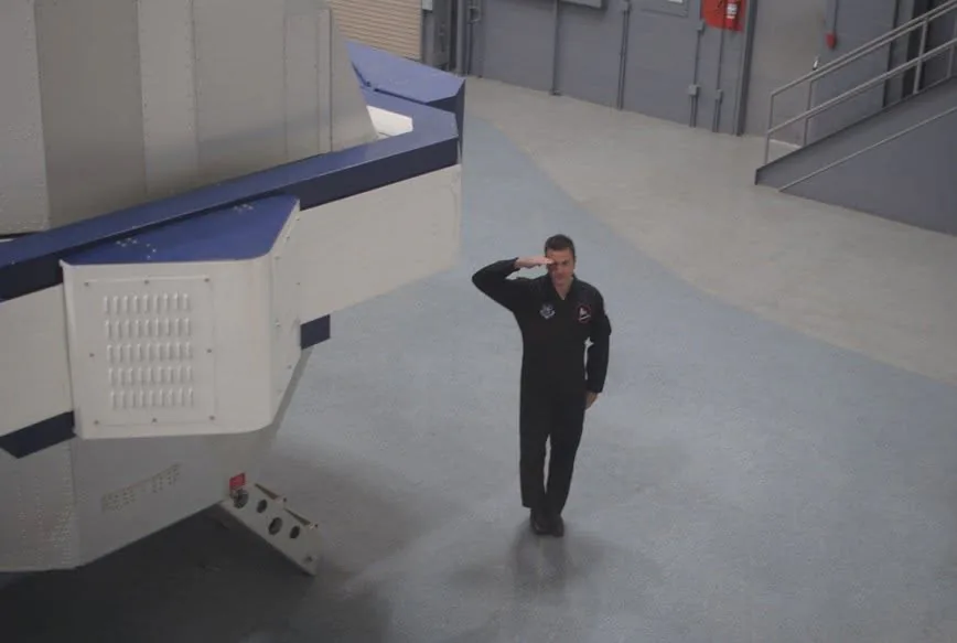 Altman in a flight suit standing beside the gondola of the high-acceleration centrifuge in the NASTAR Center training hall.